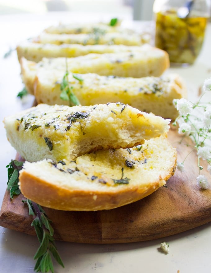 Sticks of garlic bread stacked on a cutting board with one stick bitten up