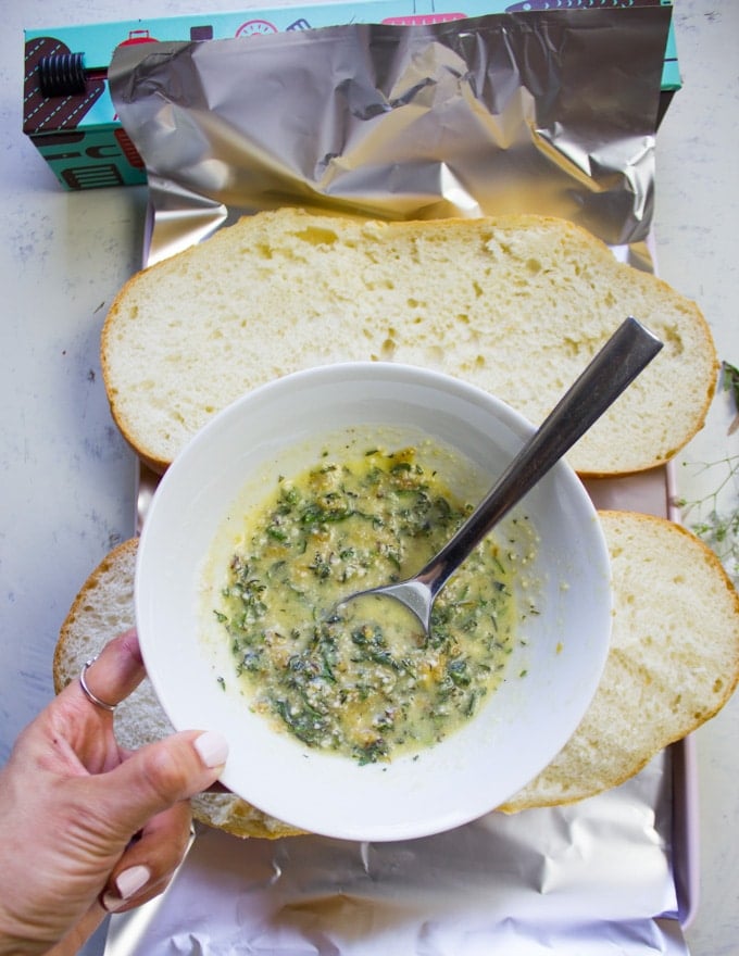 A bowl with a mixture of roasted garlic, butter, herbs and parmesan cheese ready to spread on the bread