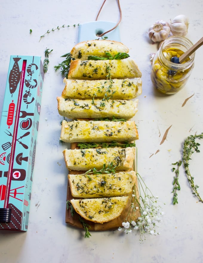 The whole loaf of garlic bread sliced on a cutting board with a jar of roasted garlic on the side