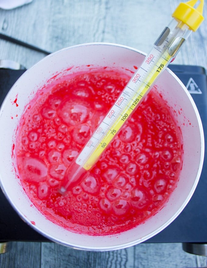 A pot showing the candy thermometer and the red sugar boiling and getting ready for the apples