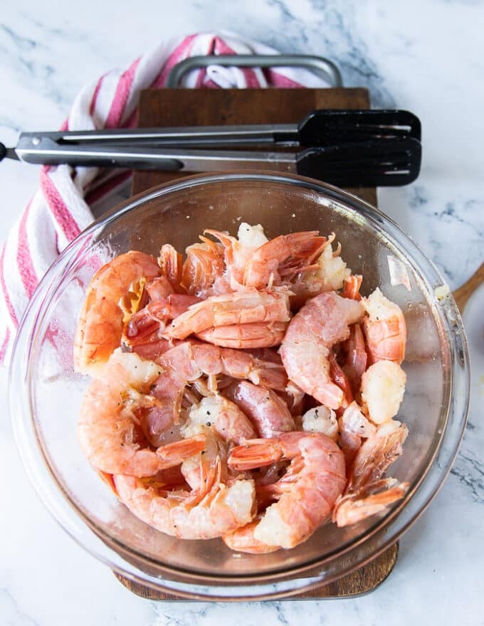 Raw shrimp in a bowl with salt, pepper and olive oil