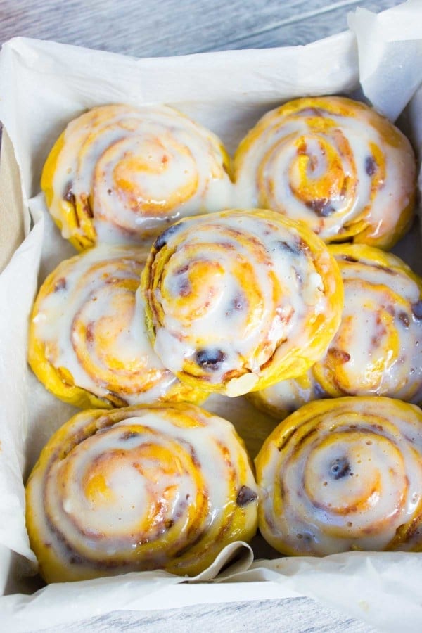 Glazed Pumpkin Cinnamon Rolls arranged in a parchment paper-lined box