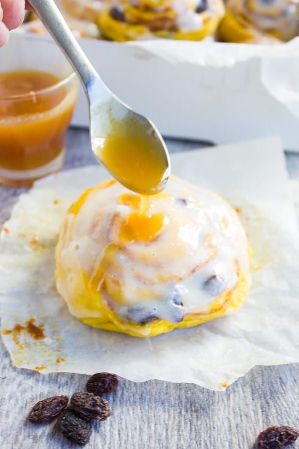 Pumpkin Cinnamon Rolls being glazed with caramel glaze