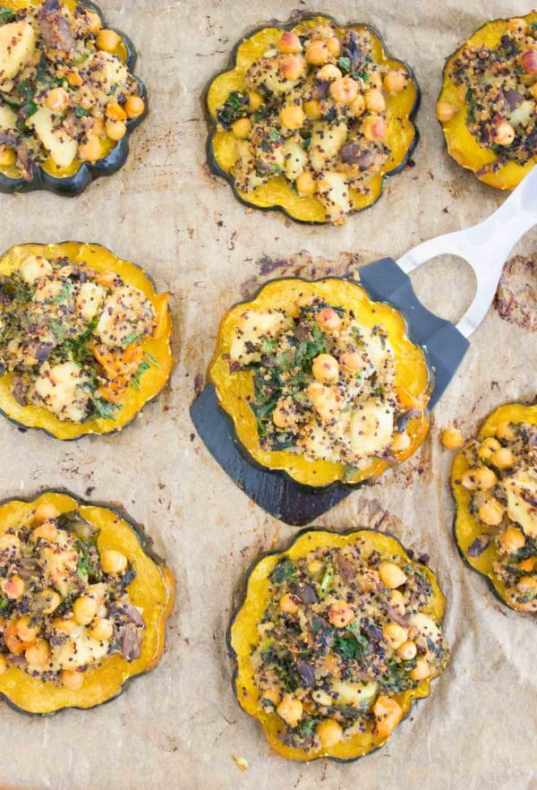 a baked acorn squash ring topped with Quinoa Kale Stuffing being lifted off a baking tray with more squash rings