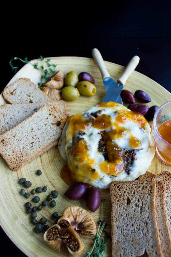 Baked Brie stuffed with Fig Olive Tapenade served on a wooden board with crackers and olives