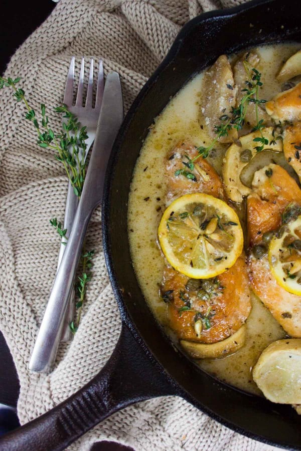 Lemon Caper Artichoke Chicken Piccata in a black skillet decorated with fresh thyme