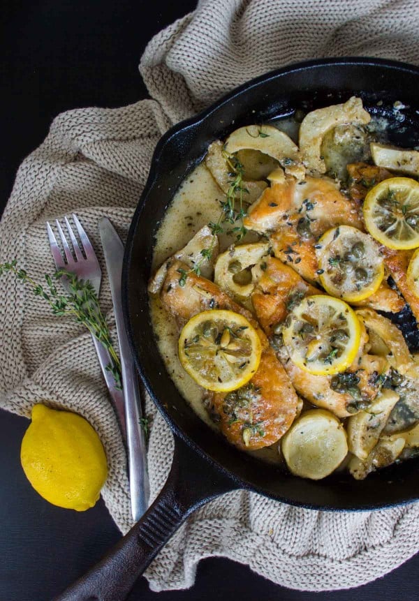 overhead of Lemon Caper Artichoke Chicken Piccata served in a black skillet with lemon and thyme twigs on the side