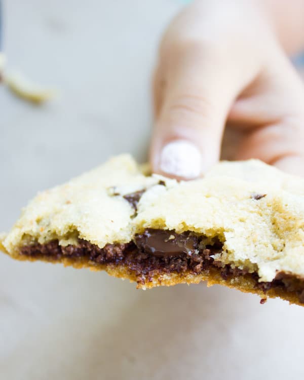 a hand holding half a Nutella-Stuffed Chocolate Chip Cookie with Nutella oozing out the middle