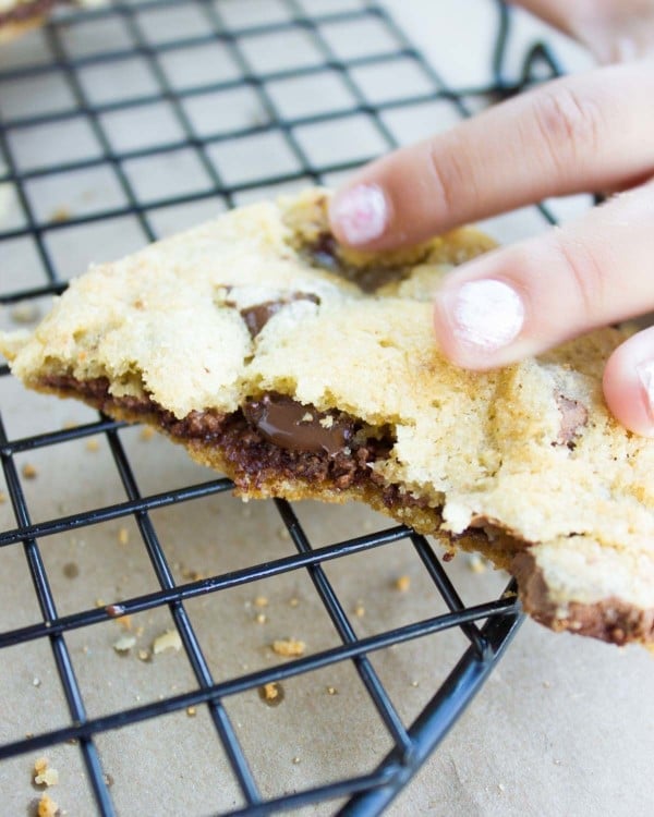 a hand reaching for half a Nutella-Stuffed Chocolate Chip Cookie on a cookie rack