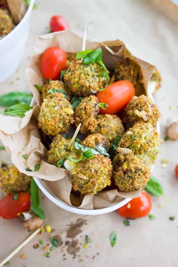 Close up image of a fried mozzarella ball coated in pistachio and skewered with a tomato and basil leaf.
