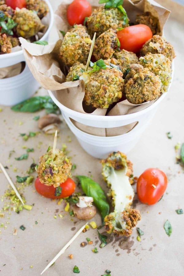 A close up image of a stretchy fried caprese bite and other stacked up caprese bites in a paper lined basket.