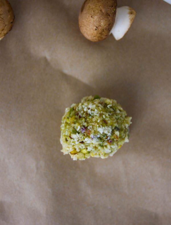 A bocconcini cheese coated in flour, pesto and pistachio ready for frying
