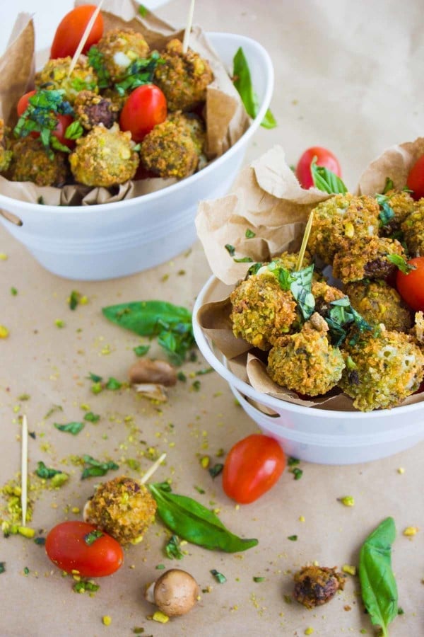 two buckets of fried mozzarella cheese in a pistachio crust, some tomatoes and fresh basil.