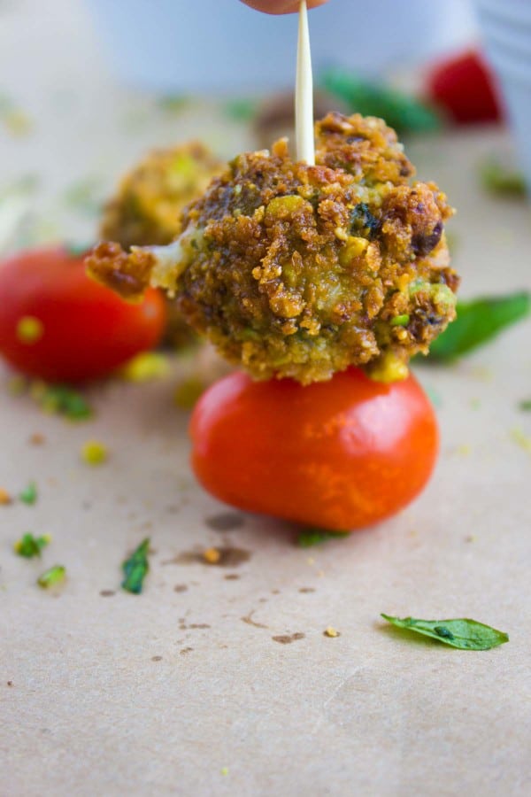 A hand holding a stick with a fried mozzarella and tomato