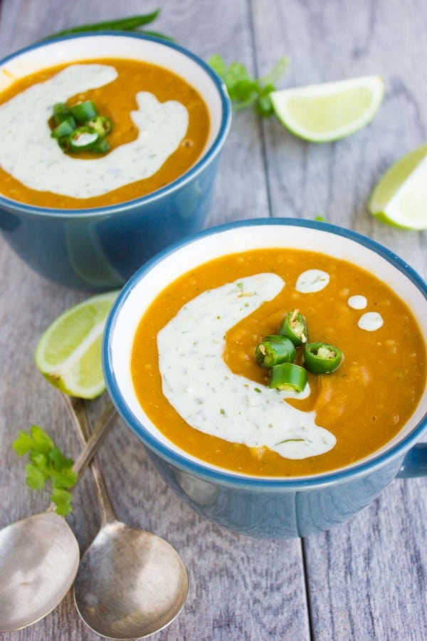 two bowl of creamy healthy lentil soup with red lentils quinoa and sweet potatoes served with a sour cream drizzle, with lime wedges on the side