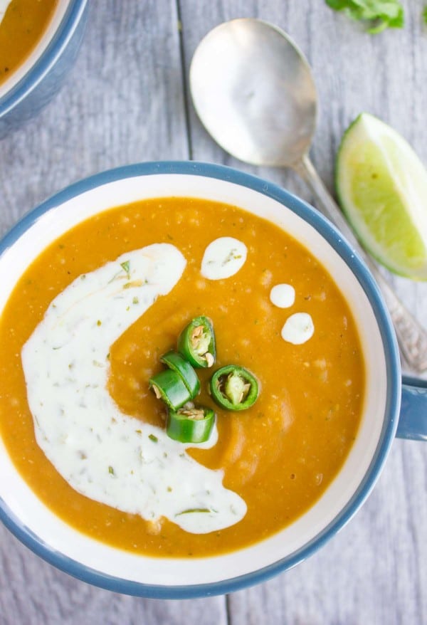 a bowl of healthy lentil soup with red lentils quinoa and sweet potatoes served with a sour cream drizzle and jalapeno slices on top