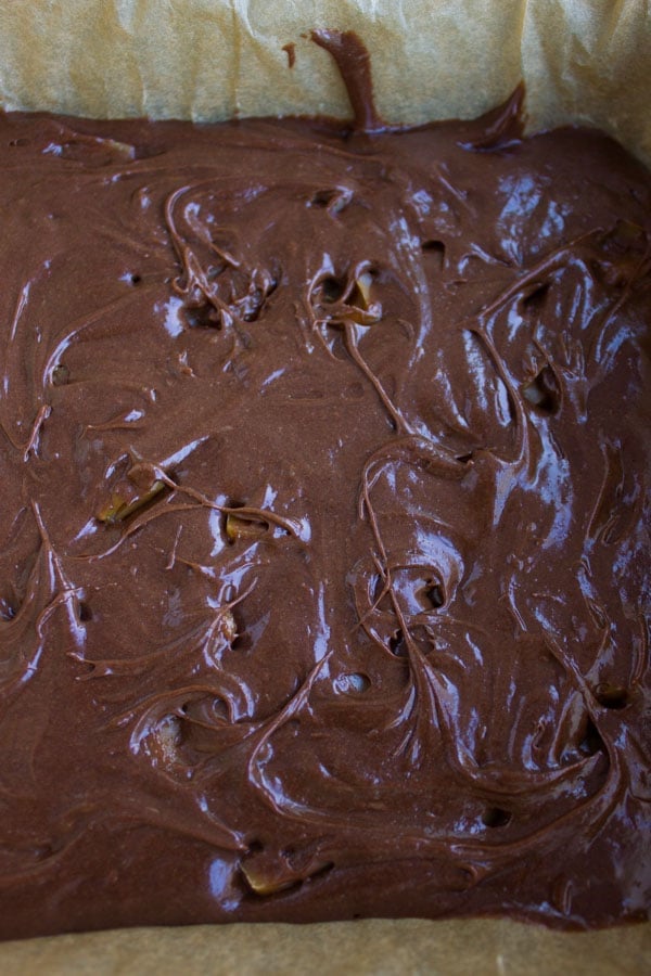 chocolate brownie batter being swirled with caramel chunks before baking