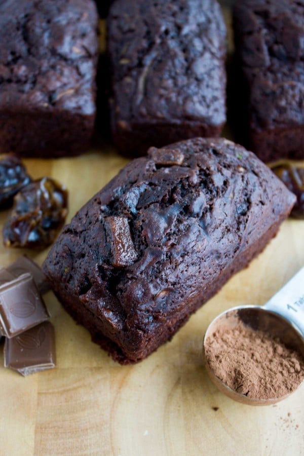 a mini loaf of Double Chocolate Date Zucchini Bread on a wooden board with some dates and cocoa powder on the side.