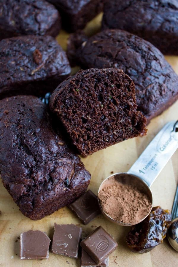  mini loafs of Double Chocolate Date Zucchini Bread on a wooden board with some dates and cocoa powder on the side.