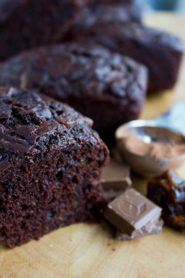 close-up of mini loaf of Double Chocolate Date Zucchini Bread on a wooden board with some dates and cocoa powder on the side.