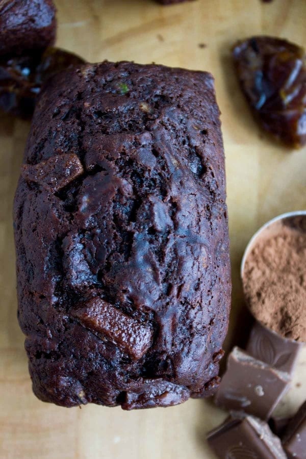 a mini loaf of Double Chocolate Date Zucchini Bread on a wooden board with some dates and cocoa powder on the side.