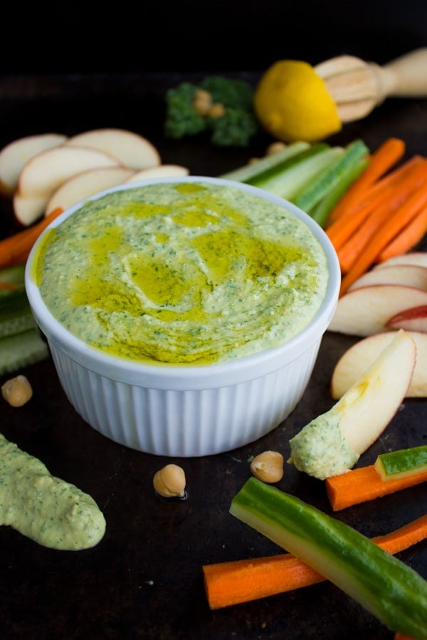Garlic Kale Hummus Dip served in a small white dish with veggie sticks in the background