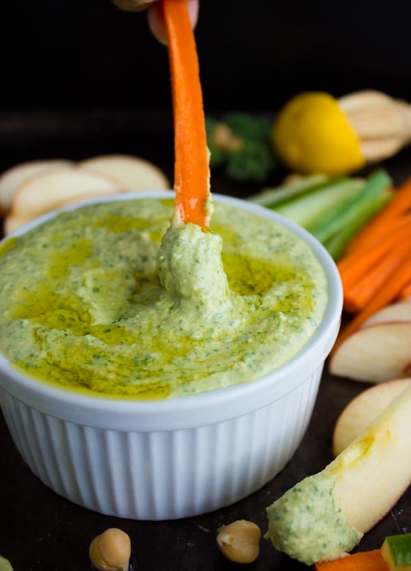 a carrot stick being dipped into a small dish of Garlic Kale Hummus Dip