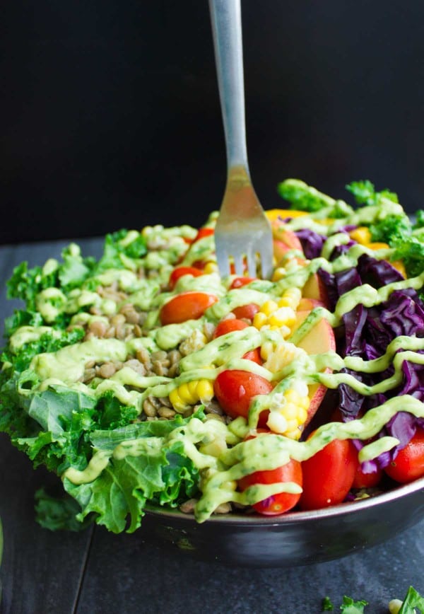 Vegan Mexican Style Lentil Detox Salad topped with fresh apples, mangoes, tomatoes and a creamy guacamole dressing served in a big salad bowl on a rustic dark wood table