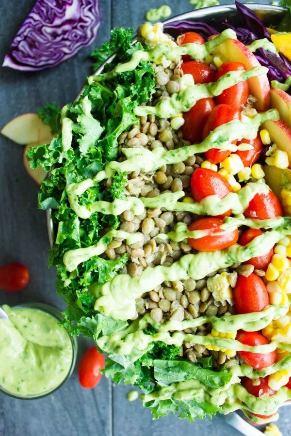 Vegan Mexican Style Lentil Detox Salad topped with fresh apples, mangoes, tomatoes and a creamy guacamole dressing served in a big salad bowl on a rustic dark wood table