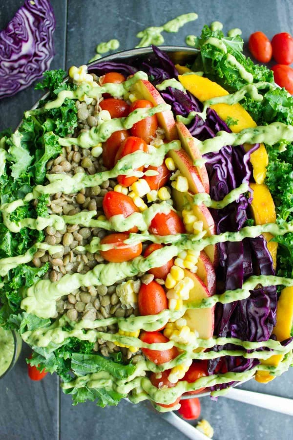 Vegan Mexican Style Lentil Detox Salad topped with fresh apples, mangoes, tomatoes and a creamy guacamole dressing served in a big salad bowl on a rustic dark wood table