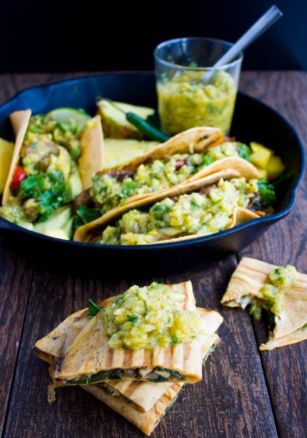 a stack of halved stuffed tortillas filled with chicken fajitas and mango pineapple salsa in front of a skillet with more fajitas