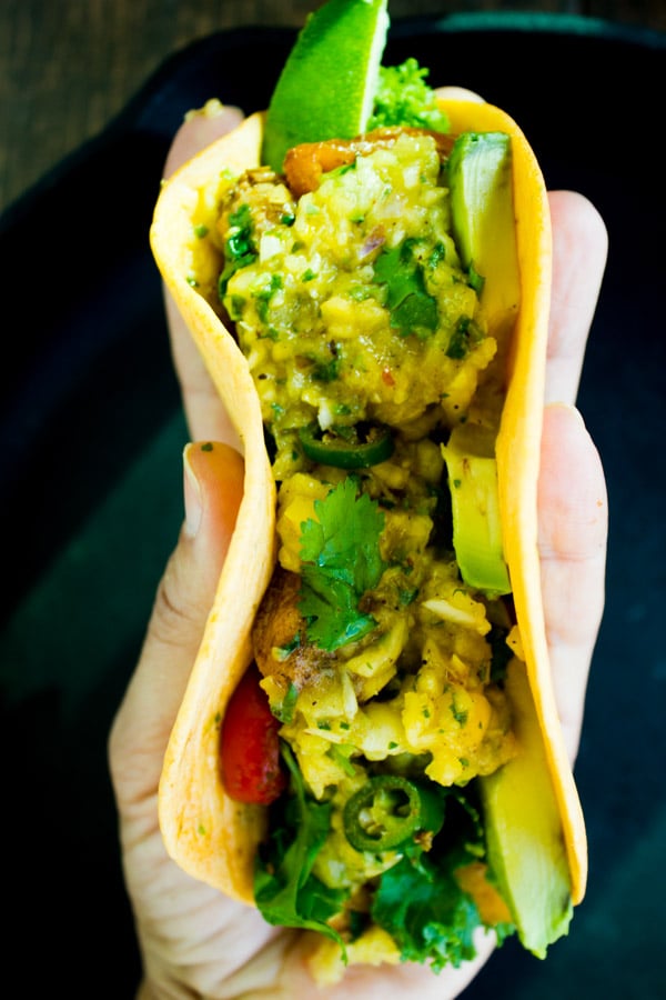 a hand holding a tortilla stuffed with chicken fajita and mango pineapple salsa