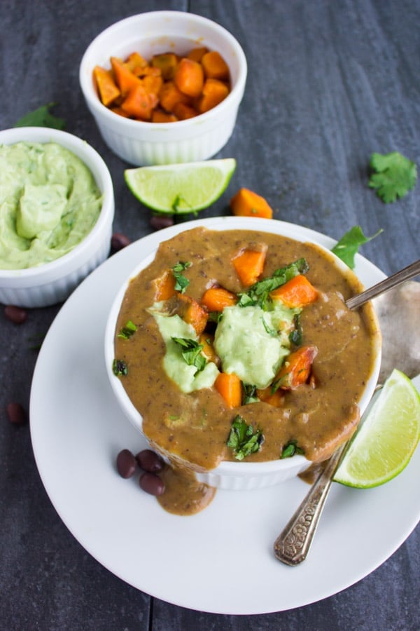 a spoon being dipped into a bowl of creamy Cuban sweet potato black bean soup making the soup spill onto the saucer