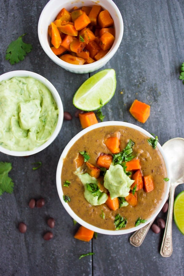 a bowl of Sweet Potato Black Bean Soup topped with cubes of roasted sweet potatoes and a dollop of avocado crema