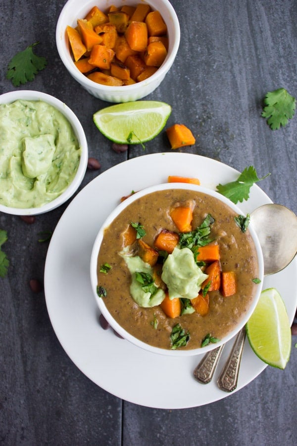 a bowl of creamy vegan Sweet Potato Black Bean Soup topped with cubes of roasted sweet potatoes and a dollop of avocado crema