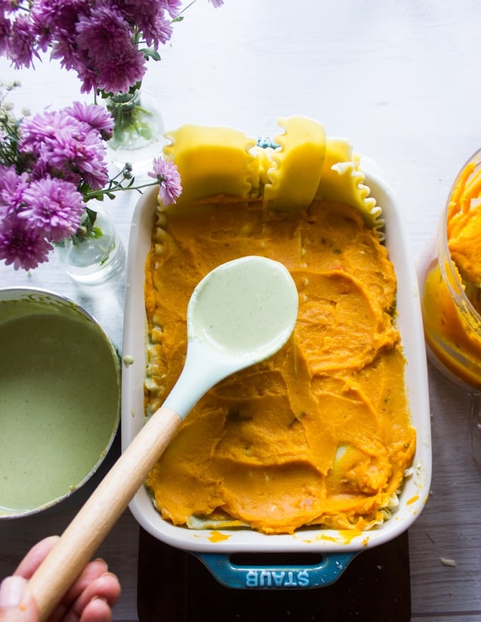 A spatula spooning over some butternut squash mixture over the lasagna sheets