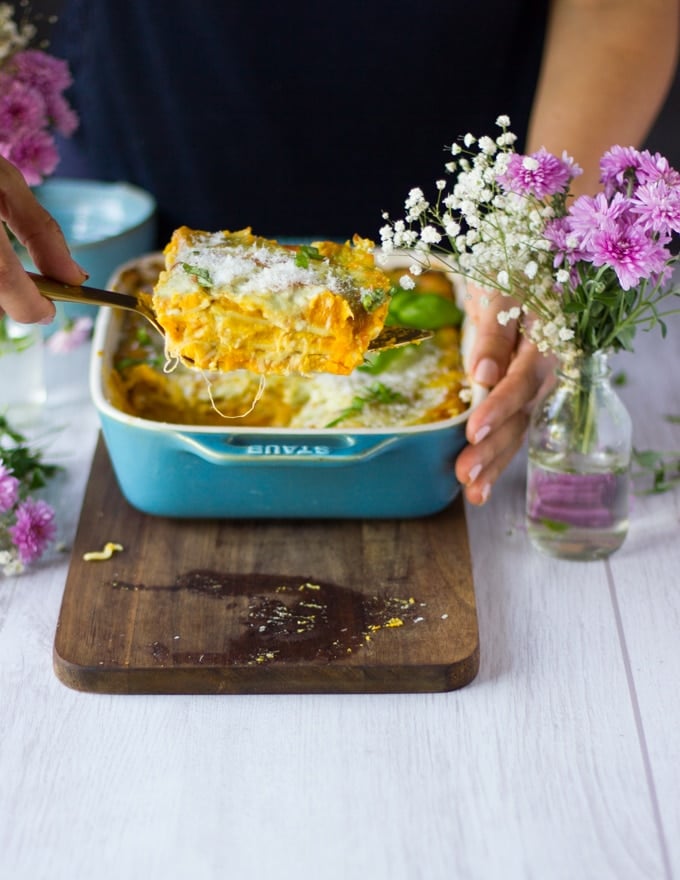 Finished off butternut lasagna out of the oven and hand trying to scoop out a slice of the lasagna on a wooden board 