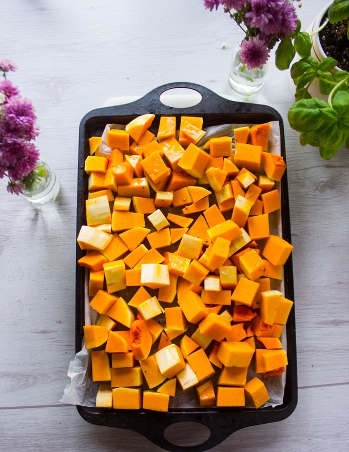 Butternut squash cut up into cubes and placed on a baking sheet, seasoned and ready for roasting