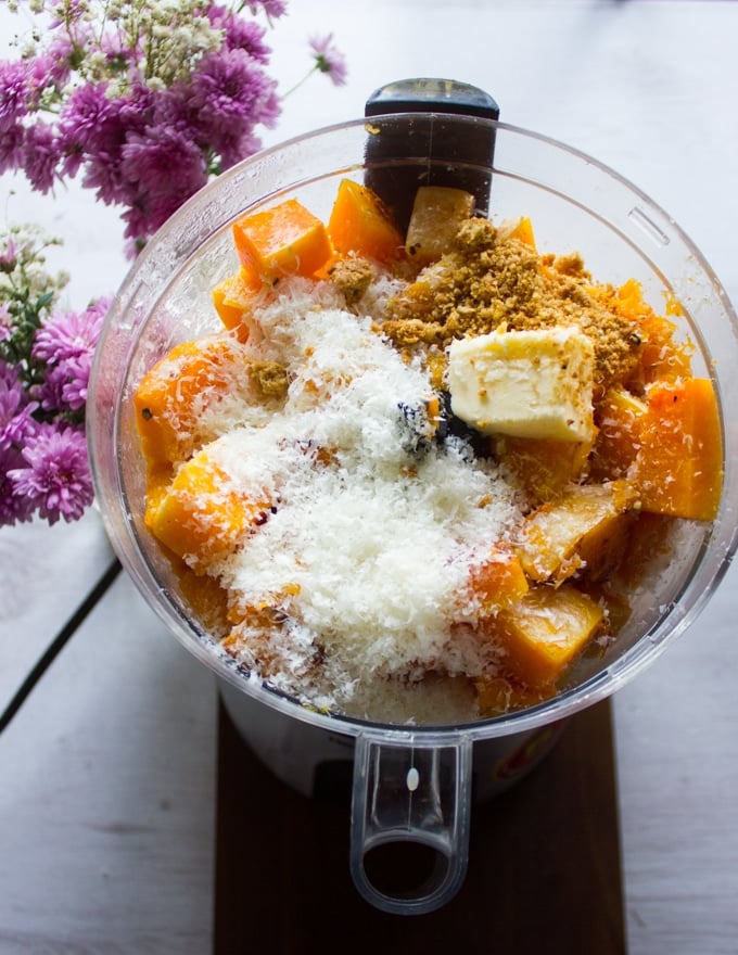 roasted butternut squash cubes in a bowl of the food processor with some butter, parmesan cheese and amaretti cookies ready to puree.