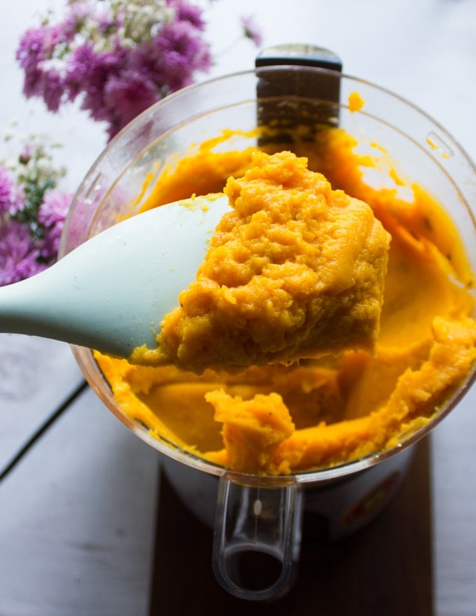 Pureed butternut squash mixture ready for the lasagna. a spatula holding the squash mixture above the bowl of a food processor showing how creamy it is!