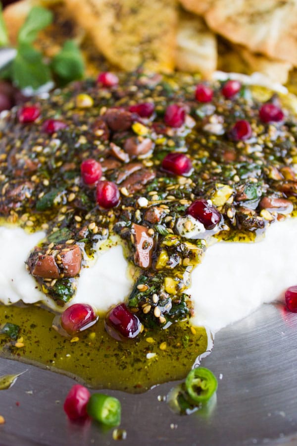 Close-up of Labneh Dip with Zaatar Pistachio Mint Olive Topping running down the sides and a pool of olive oil gathering in front of it.