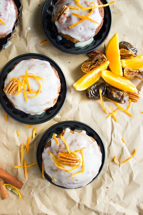 overhead shot of orange chai spice date muffins glazed with cream cheese icing and topped with orange zest and pecans