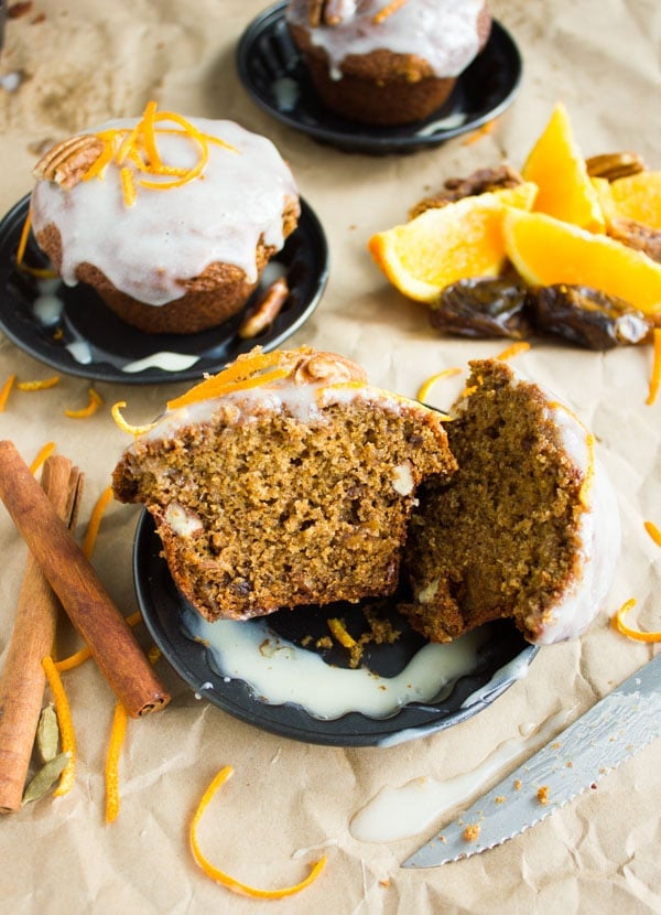 half a Orange Chai Spice Date Muffin on a small plate topped with cream cheese icing an orange zest