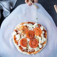 adding tomatoes to the top of a pizza.