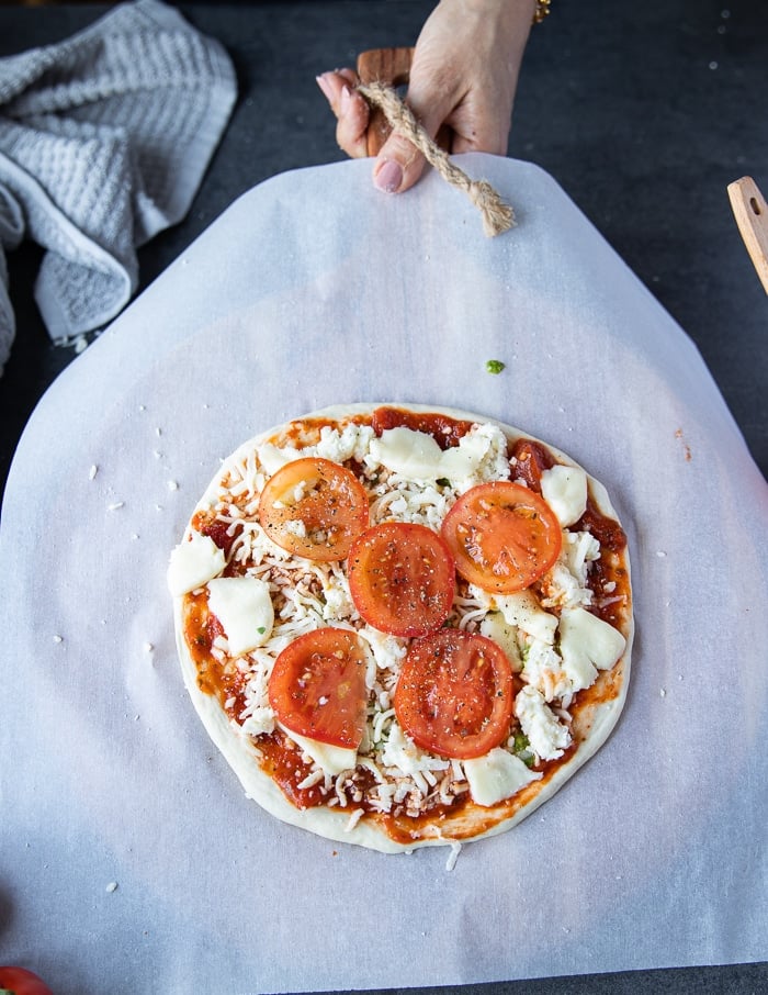 adding tomatoes to the top of a pizza.