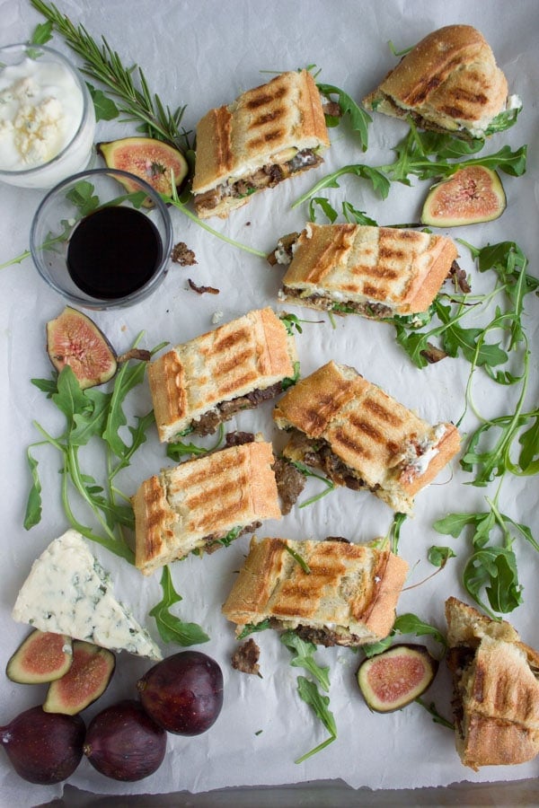 bite-sized pieces of Blue Cheese Philly Steak Sandwich arranged on parchment paper with fresh figs, blue cheese and arugula surrounding them