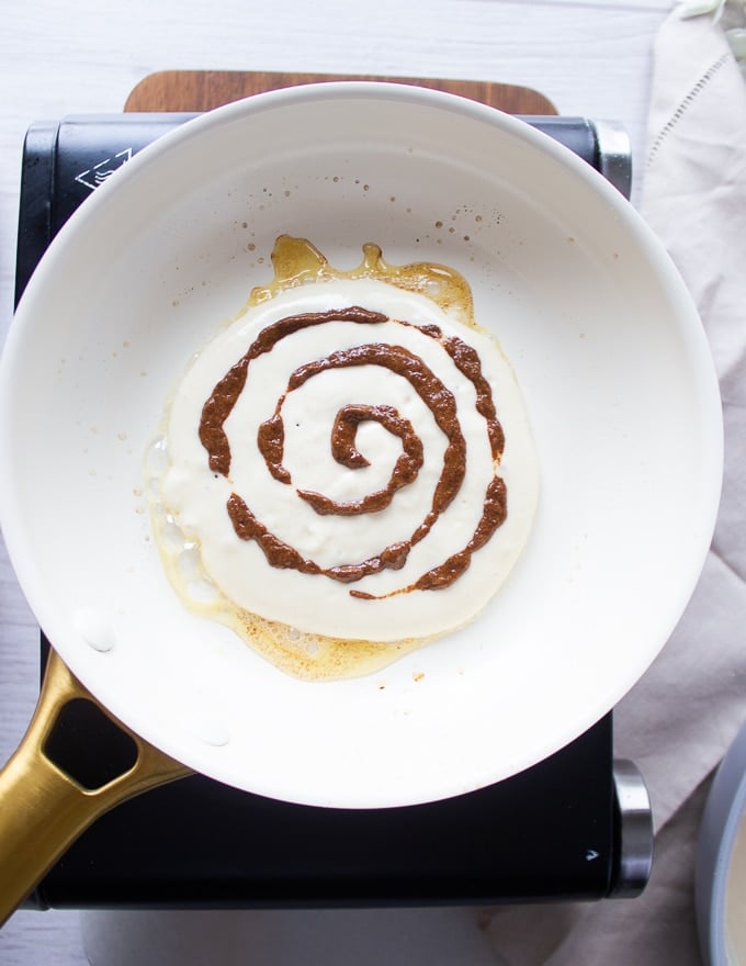 a pancake batter on a skillet and a swirl of cinnamon sugar around it
