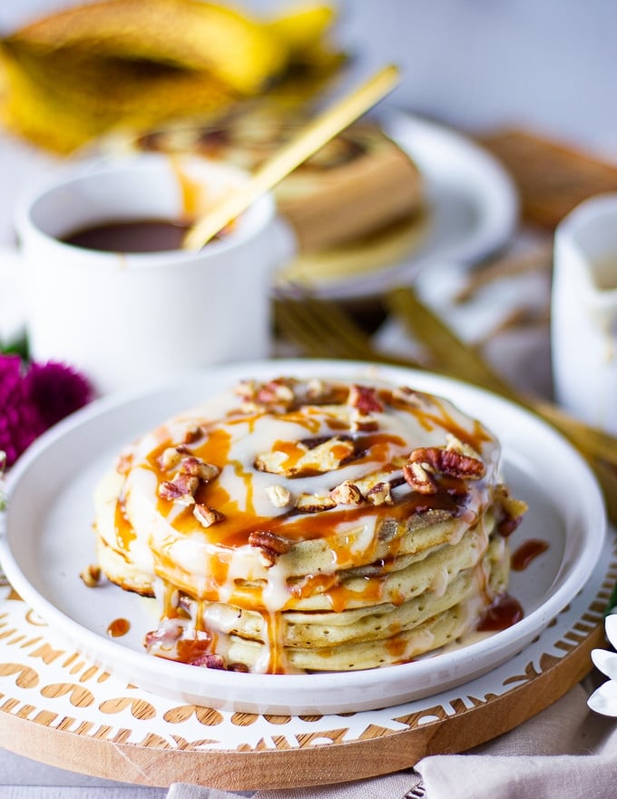 a stack of cinnamon rolls pancakes and some pecans sprinkled on top