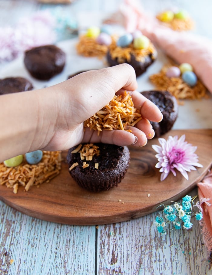 a hand pressing down toasted coconuut flakes over the coconut brownies