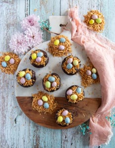 coconut brownies on a wooden board all topped and ready with coconut shreds and chocolate eggs